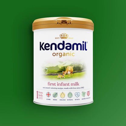 A can of Organic First Infant Milk on a green background, featuring a gold lid, a cow illustration, and icons highlighting its benefits such as being an organic whole milk formula made from grass-fed cows and suitable for use from birth.