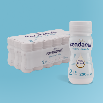 Six bottles of Kendamil 18x250ml Classic Follow-On Ready to Feed, a whole milk formula made from grass-fed cows and enriched with plant-based DHA, are displayed with one bottle in the foreground. Each is labeled for ages 6-12 months and contains 250 ml. The background is light blue.
