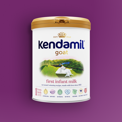 A can of Kendamil Goat First Infant Milk with a gold lid, featuring an illustration of goats in a field and icons indicating suitability from birth, no palm oil, no fish oil, vegetarian-friendly, and full cream nutrients.